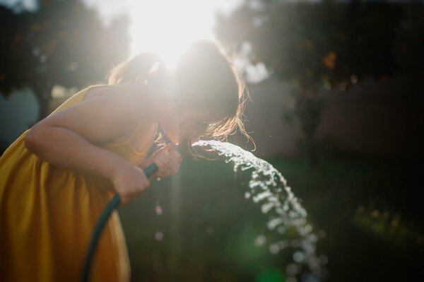 Ragazza che beve acqua da un tubo in estate