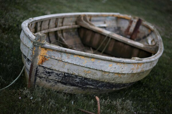 Старая выцветшая лодка стоит на зелёной траве