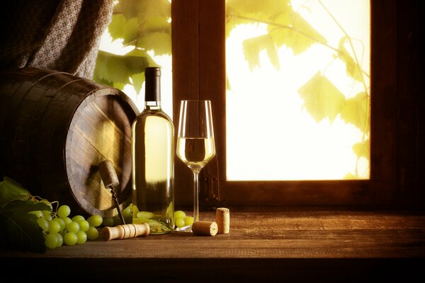 On the windowsill there is wine, a glass, grapes and a barrel