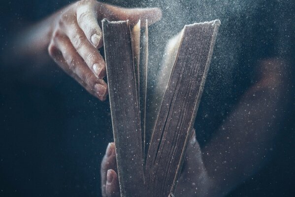 Ręce trzymają starą książkę z której wylatuje kurz