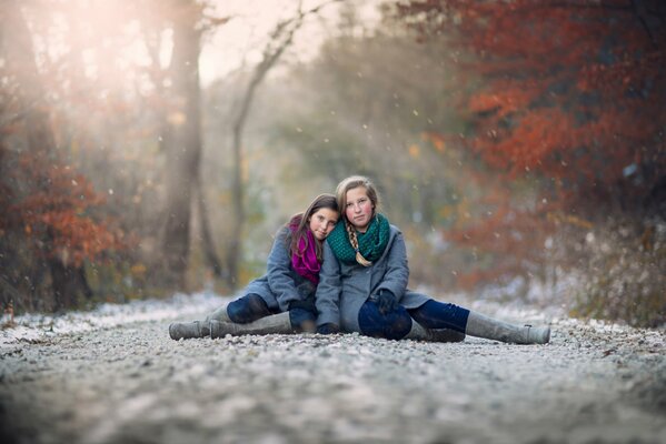 Le ragazze si siedono di lato nella neve in autunno