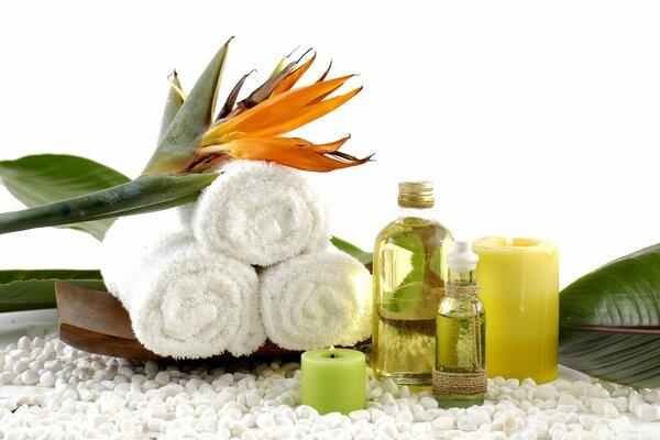 Burning candles on pebbles and next to oil and towels on which a flower