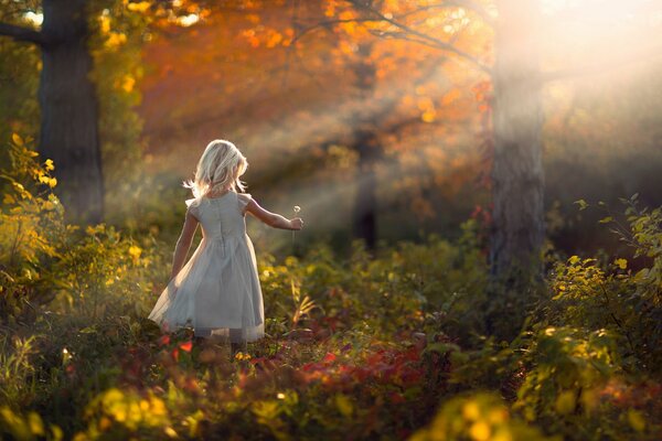 A girl with a dandelion in her hands in the autumn forest