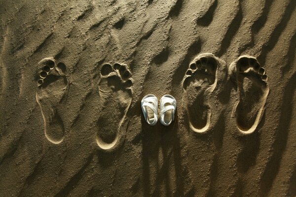 Fußabdrücke der Eltern und Schuhe des Kindes im Sand