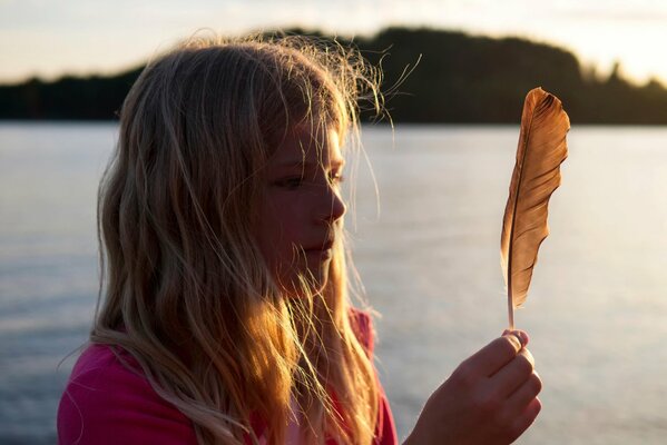 Una niña en el sol Mira una pluma