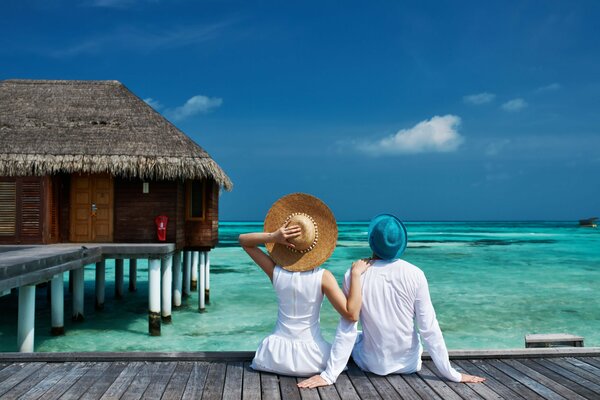 A couple in white are sitting on the path to a bungalow in the sea