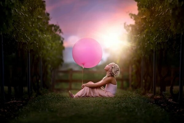 Funny girl sitting on the grass and holding a pink ball