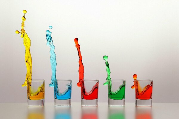 Multicolored liquids splash out of the glasses merrily