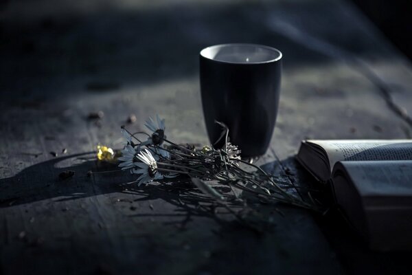 Flowers with a mug on the table along with a book