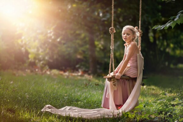 Fille en robe tranquillement assis sur une balançoire au soleil d été fond d écran