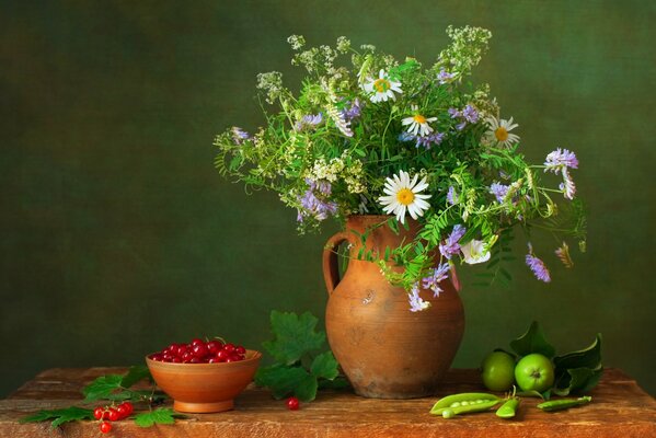 Still life on the table there is a jug with a bouquet of flowers and berries and apples around