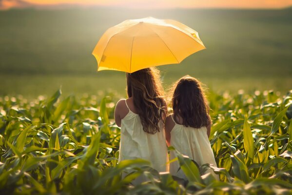 Madre e hija bajo un paraguas amarillo en el maíz