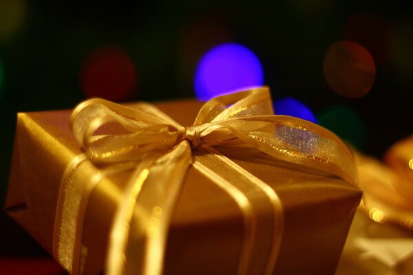 Gift box in a golden package with a golden bow on a background of multicolored spots of light