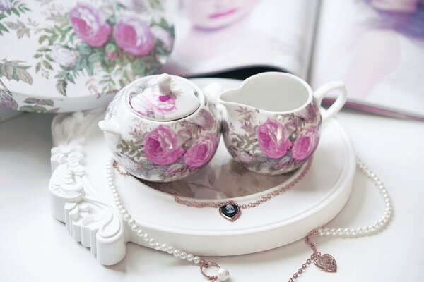 Juego de té con rosas y collar sobre fondo blanco