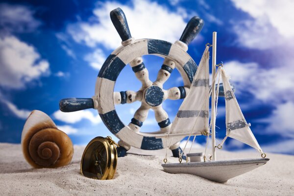Coquillage, boussole, gouvernail et bateau sur le sable
