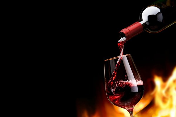 Aus einer Flasche Rotwein fließt Wein in ein Glas hinter der Flamme