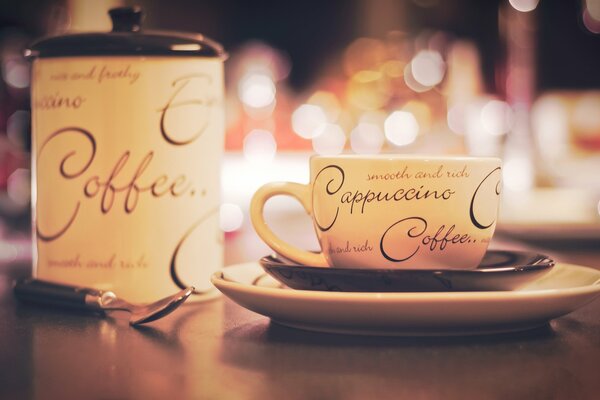 Eine Tasse Cappuccino zusammen mit einer Zuckerdose auf dem Tisch. Foto mit Bokeh-Effekt