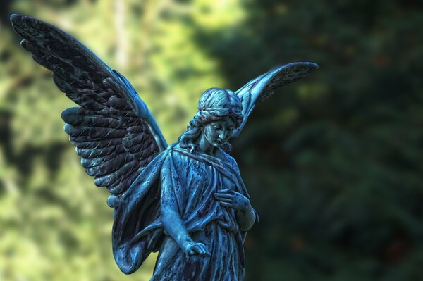 Posąg anioła ze skrzydłami na tle drzew