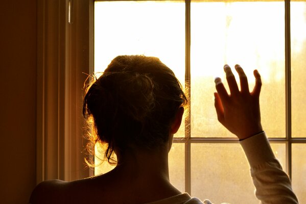 Jeune fille, avec la main levée, regarde par la fenêtre