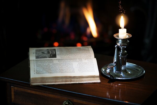 There is a candle in a candlestick and an open book on the bedside table