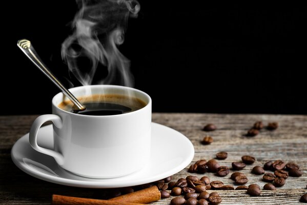Una taza de café caliente y fragante se encuentra sobre una mesa en la que se dispersan granos de café y canela