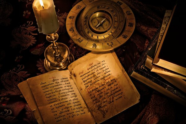Stara książka z kompasem przy świecy na stole Tapeta