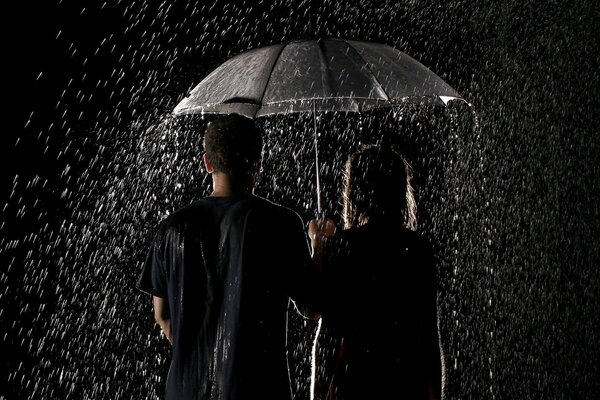 A couple of lovers are standing in the rain under an umbrella