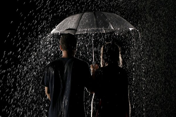 Pareja de enamorados de pie bajo la lluvia bajo un paraguas