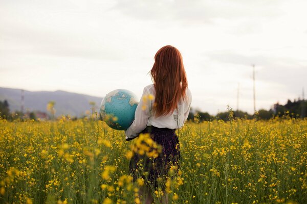 Foto di una ragazza dai Capelli rossi con un globo in mano in un campo di colza