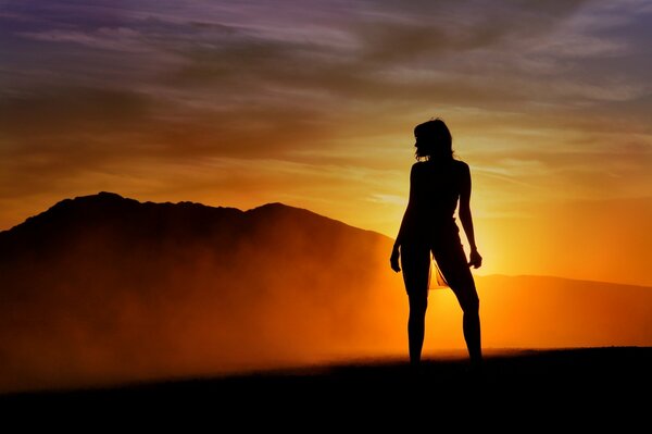 Hermosa silueta de una niña en el fondo de la puesta de sol y las montañas