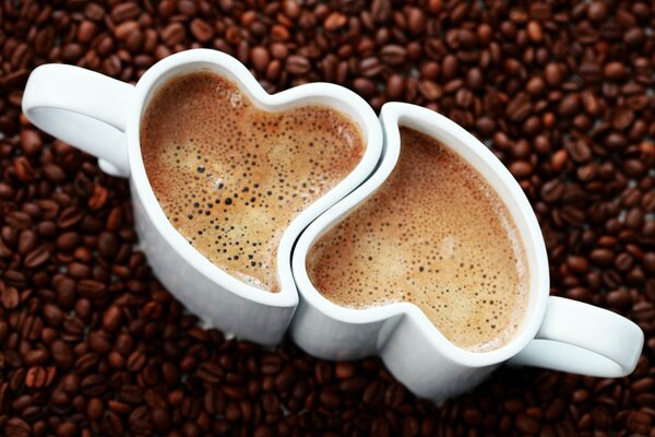 Deux tasses de café avec forme de coeur sur fond de grains de café