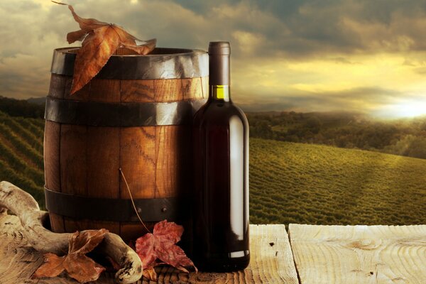 A dark bottle of wine next to an oak barrel against the background of long vineyards in the sunset of the autumn Sun