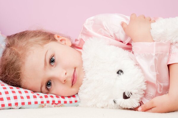 Picture of a girl lying on a pillow in an embrace with a bear