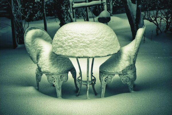 Snow-covered chairs and a table on a frosty day outside