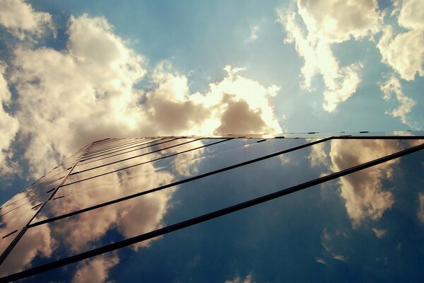 A mirrored skyscraper reflects the sky and clouds