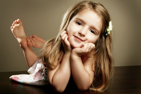 A baby girl lies and poses for a photographer with a hairpin bow