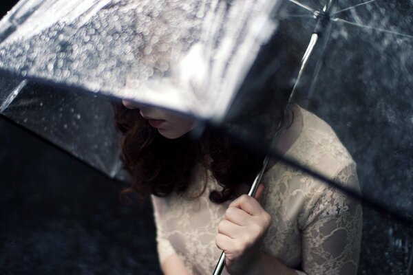 Fille se cache de la pluie sous un parapluie transparent