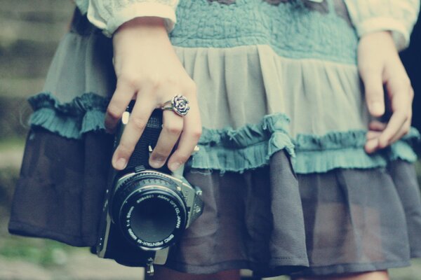 A girl in a blue dress with a camera in her hands and a ring on her finger