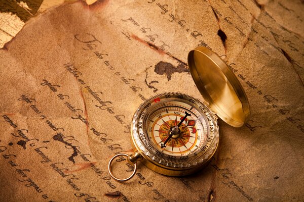 Auf den alten Aufzeichnungen liegt ein Kompass, sein Pfeil zeigt die Richtung nach Süden an
