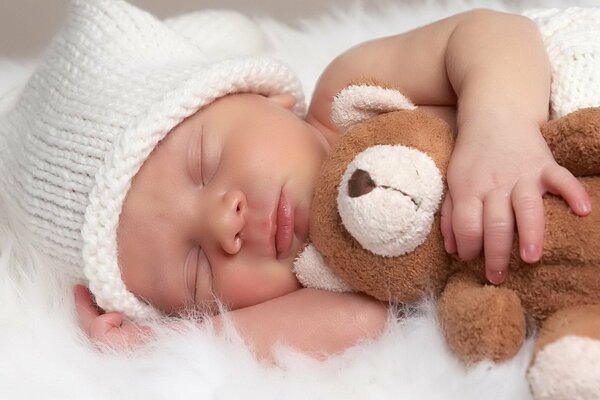 Bambino addormentato in un cappello con un orsacchiotto