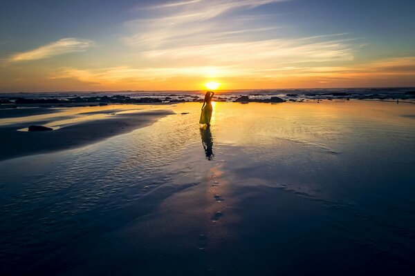 A girl in a light dress on the beach with the setting sun