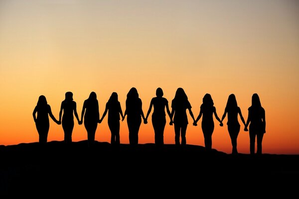 Dark silhouettes of women holding hands against the background of a bright sunset