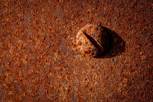 A red rusty metal bolt is lying