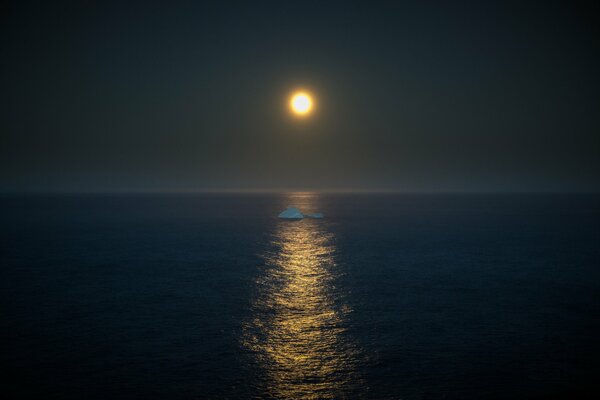 An iceberg floats in the middle of the sea in the light of the full moon