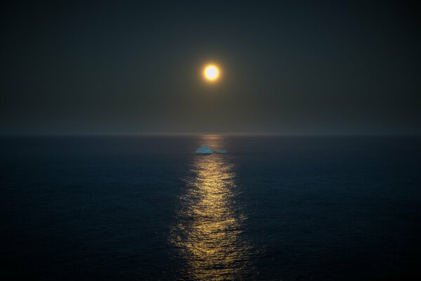 Au milieu de la mer à la lumière de la pleine lune flotte un iceberg