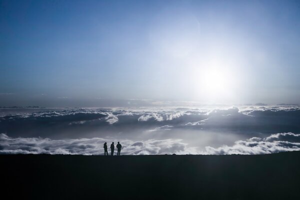 La gente en la montaña a la par con las nubes bajo los rayos del sol