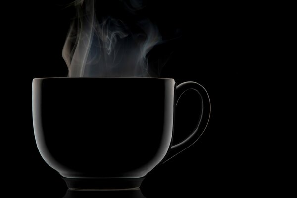 Taza negra de la que viene el vapor sobre un fondo negro