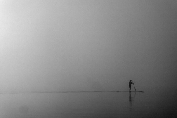 Uomo nella nebbia impegnato nel sapsurfing sul mare