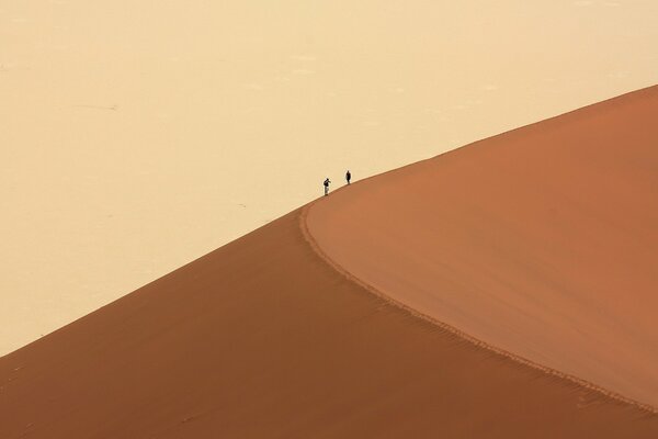 Dos personas suben una duna en el desierto