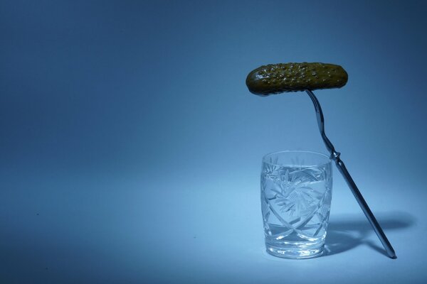 A shot of vodka and a cucumber on a blue background